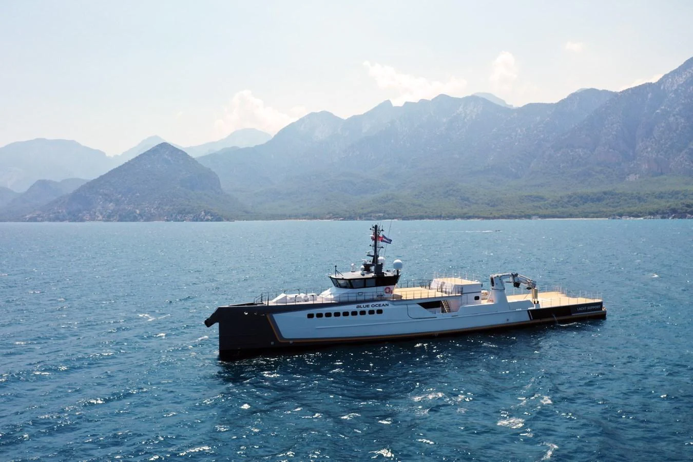 A sleek yacht cruises on calm waters with a mountainous backdrop. aboard GENE CHASER Yacht for Sale