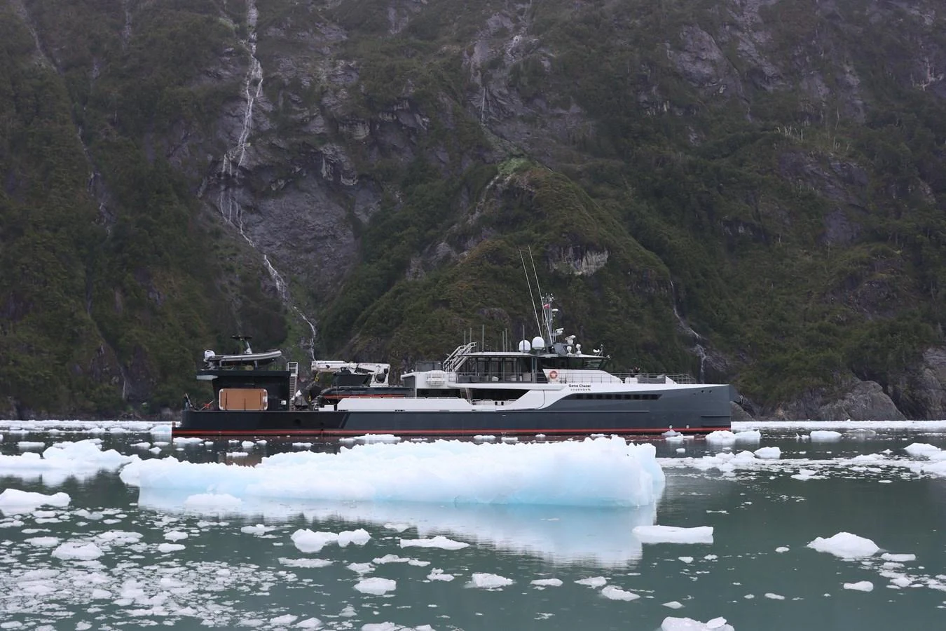 The yacht is cruising through icy waters with a rugged mountainous backdrop. aboard GENE CHASER Yacht for Sale