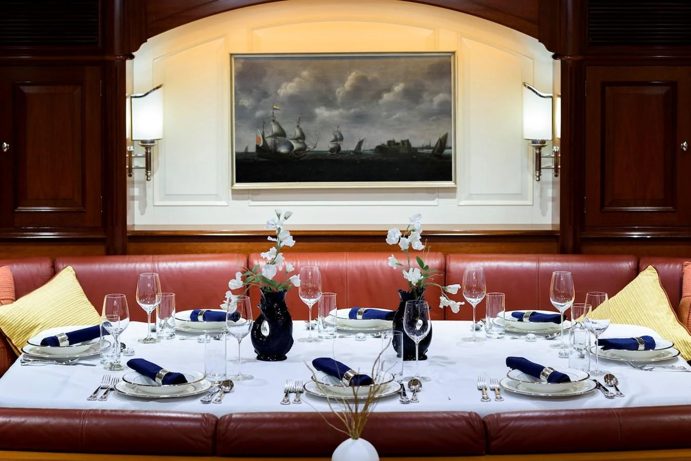 The yacht's dining area features an elegant table setting with fine china and glassware, complemented by a classic maritime painting. aboard METEOR Yacht for Sale