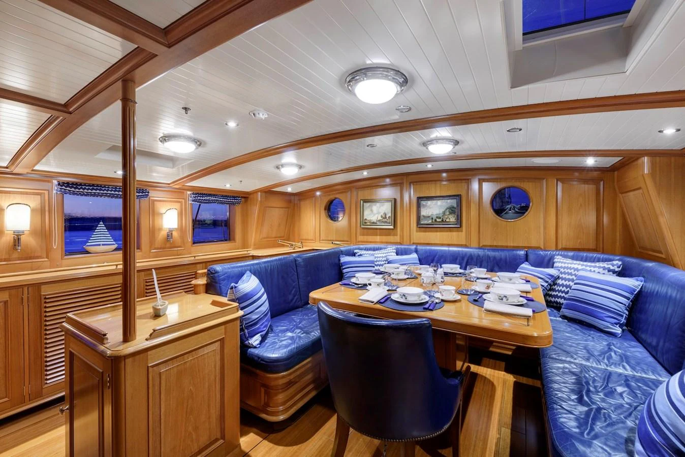 The yacht's dining area features a cozy and elegant setting with a large wooden table surrounded by plush blue seating. aboard METEOR Yacht for Sale