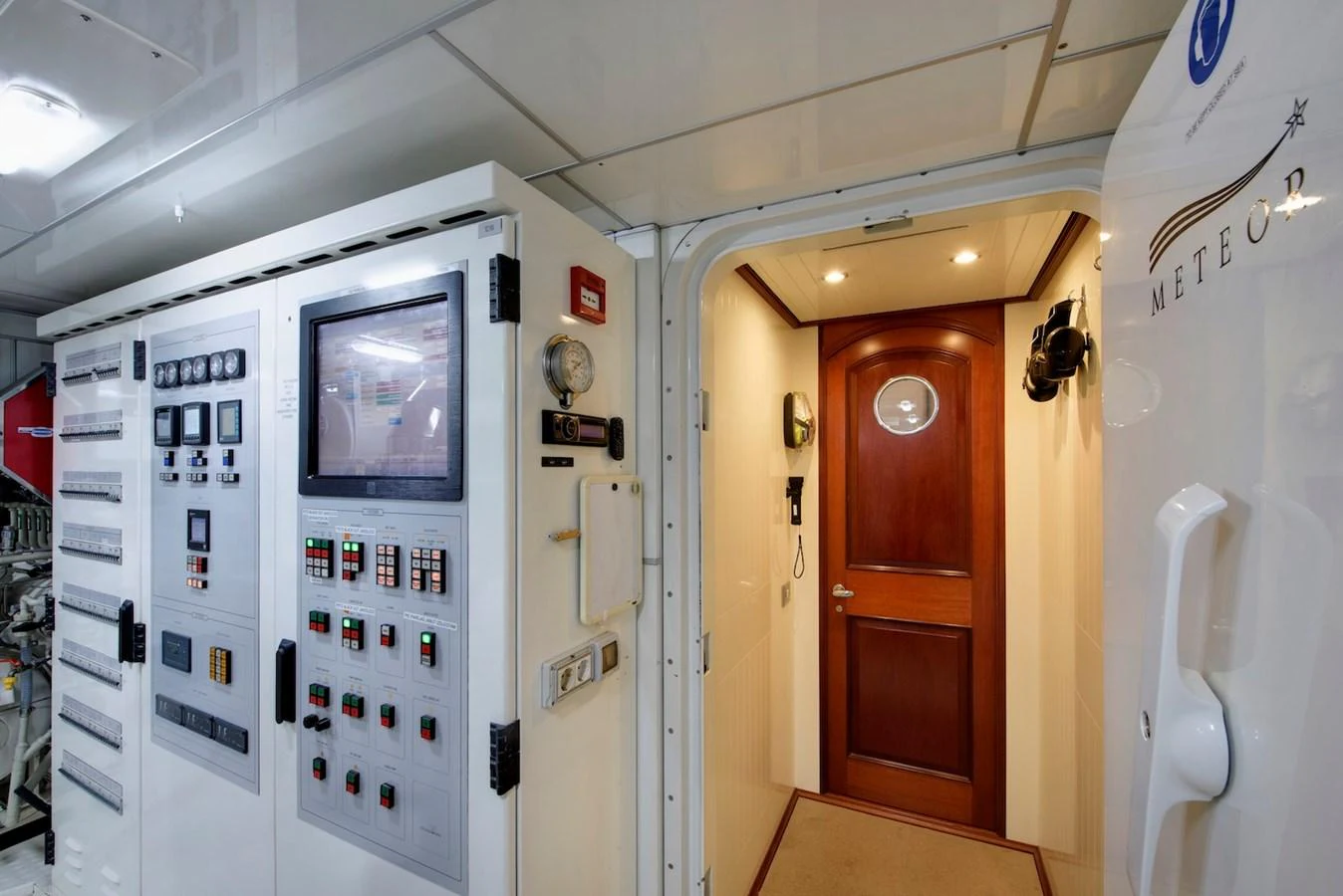 The image showcases the yacht's well-equipped engine room with advanced control panels and a wooden door leading to another section. aboard METEOR Yacht for Sale