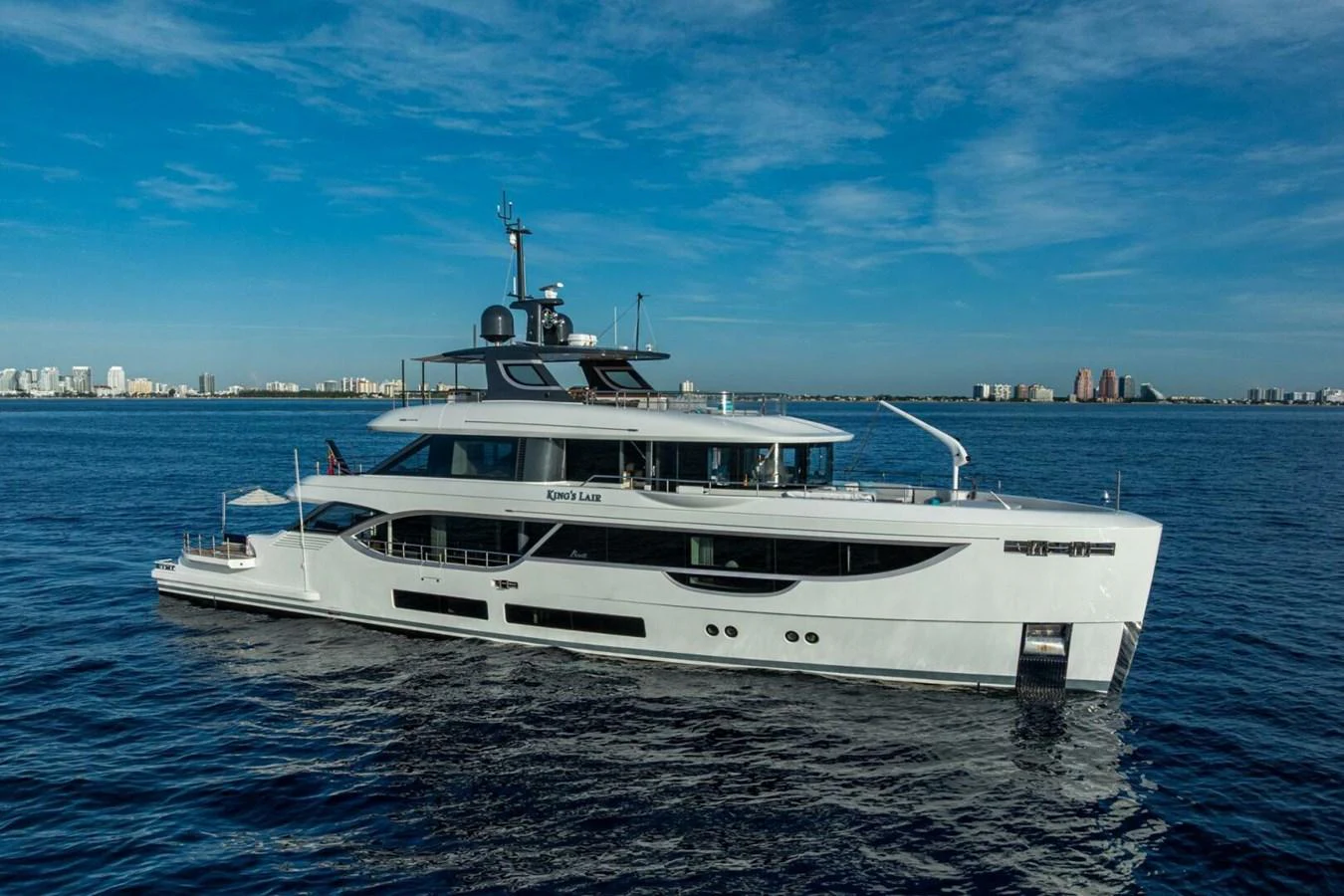 A sleek and modern yacht glides gracefully on calm waters with a cityscape in the background. aboard KING'S LAIR Yacht for Sale