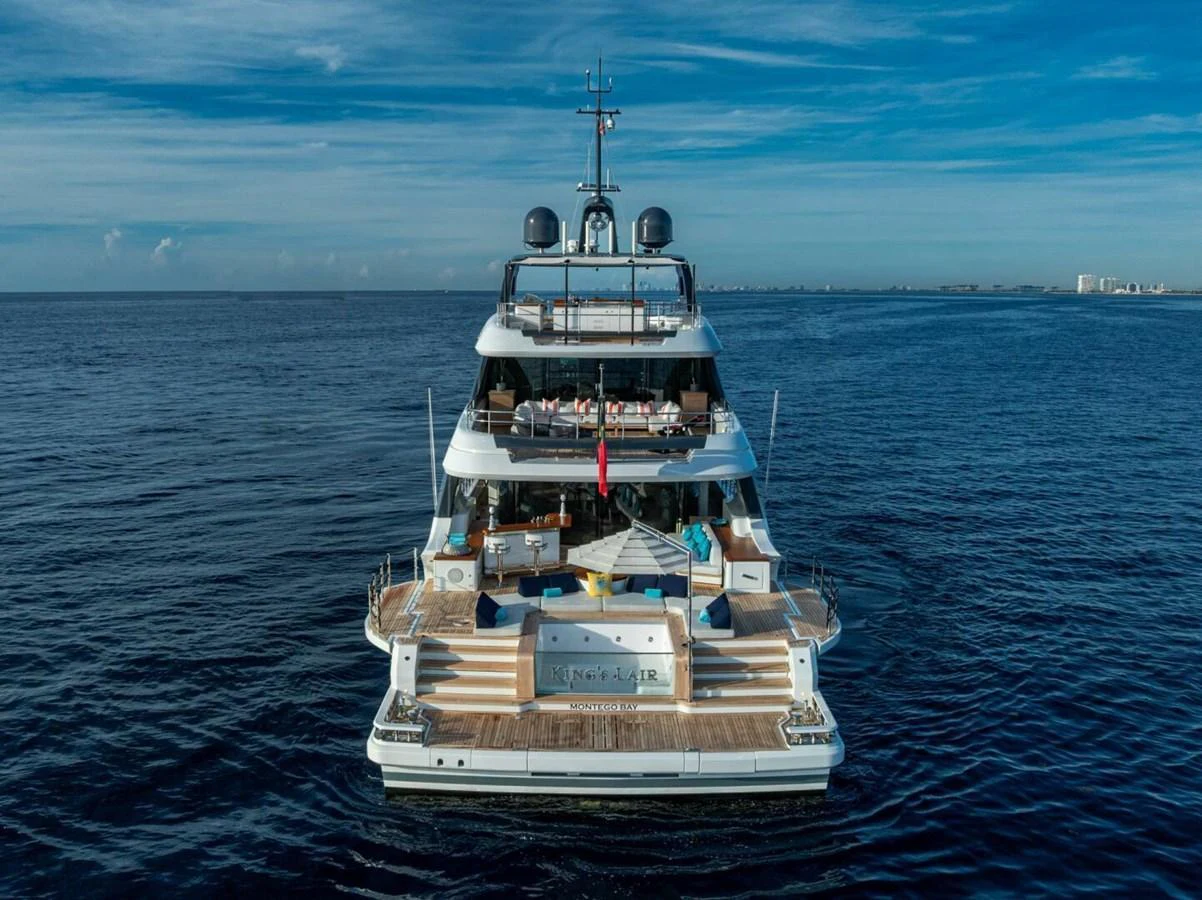A luxurious yacht is anchored on calm waters, showcasing its expansive aft deck and multiple levels of outdoor living spaces. aboard KING'S LAIR Yacht for Sale