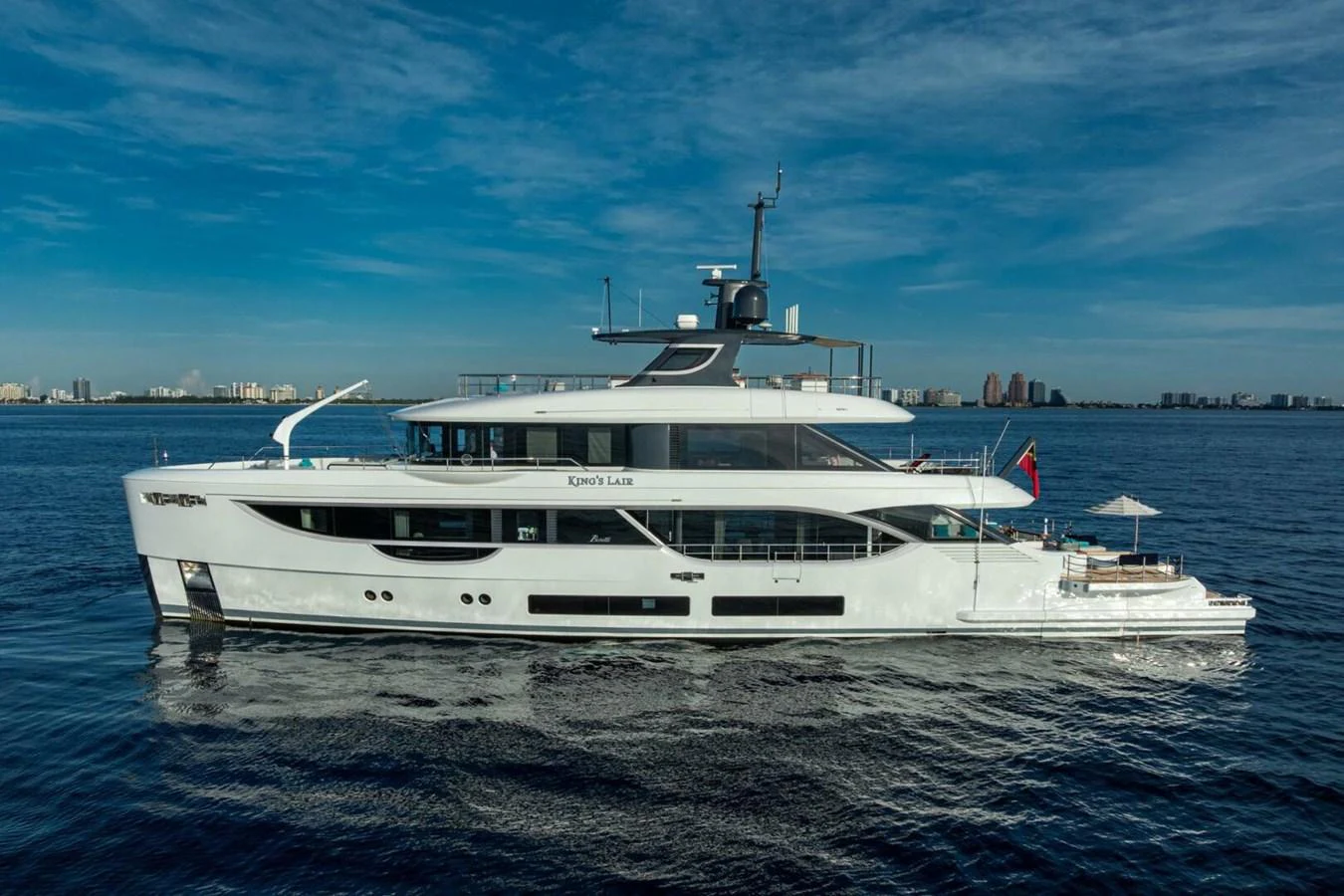 A sleek and modern yacht cruising on calm waters with a cityscape in the background. aboard KING'S LAIR Yacht for Sale