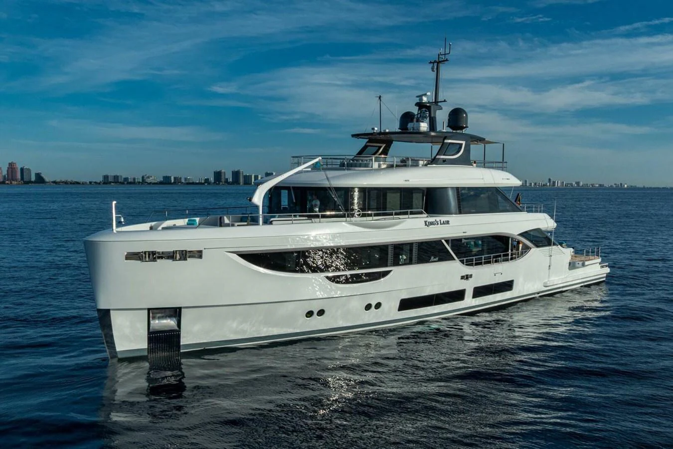 A sleek and modern yacht glides gracefully on calm waters with a cityscape in the background. aboard KING'S LAIR Yacht for Sale
