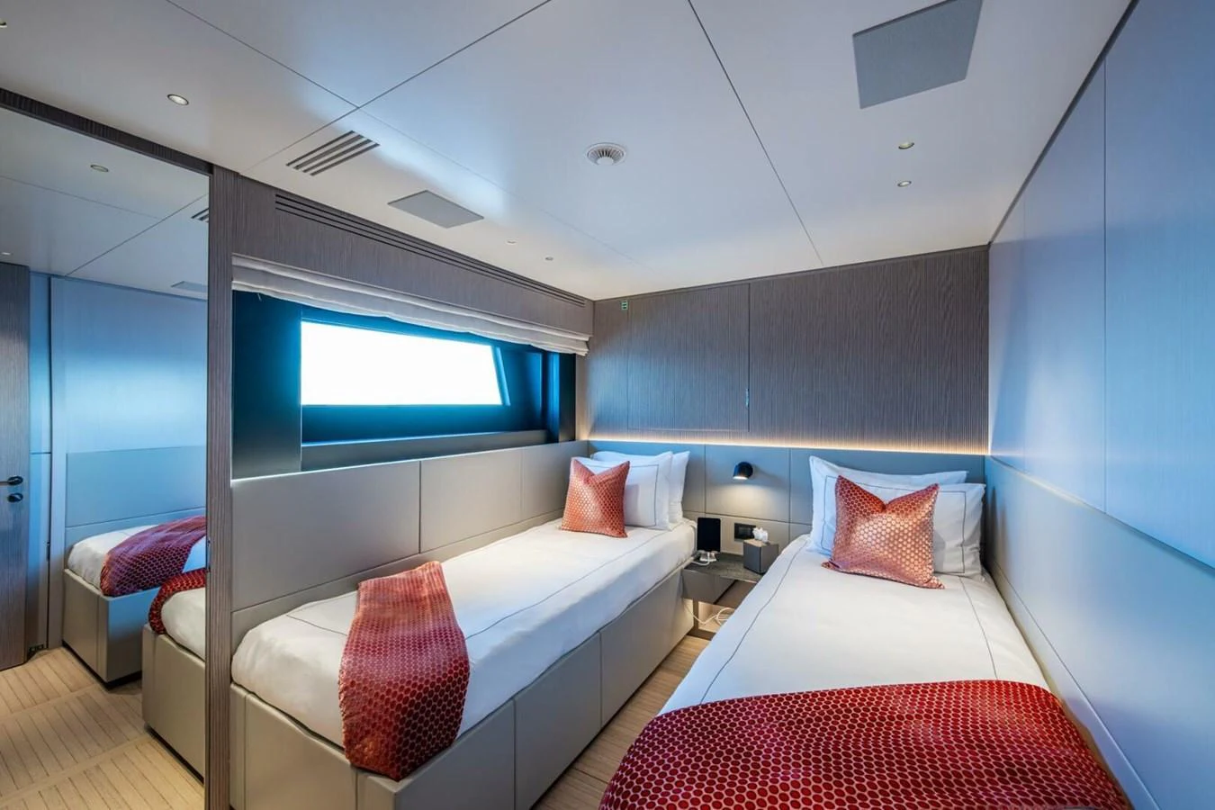 The guest stateroom features two single beds with elegant red accents and a large window for natural light. aboard KING'S LAIR Yacht for Sale