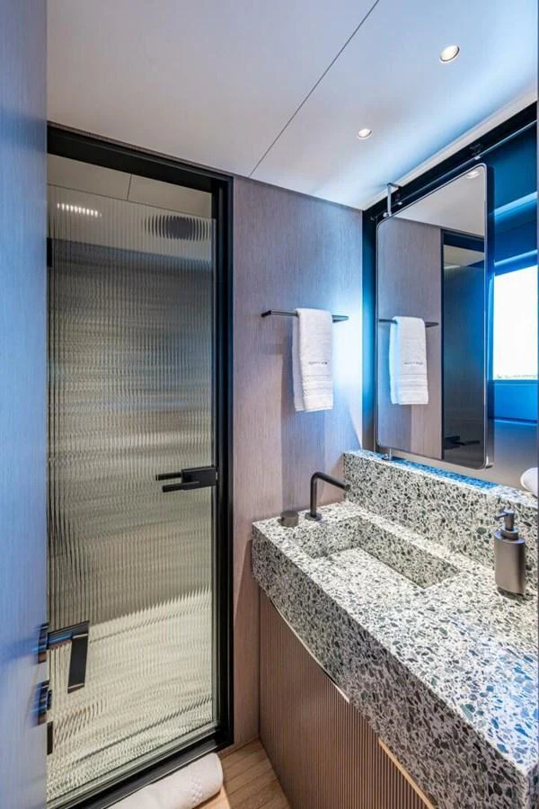 A modern yacht bathroom featuring a sleek design with a granite countertop and a glass shower door. aboard KING'S LAIR Yacht for Sale