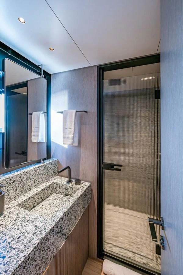 A modern yacht bathroom featuring a sleek granite countertop and a glass shower enclosure. aboard KING'S LAIR Yacht for Sale
