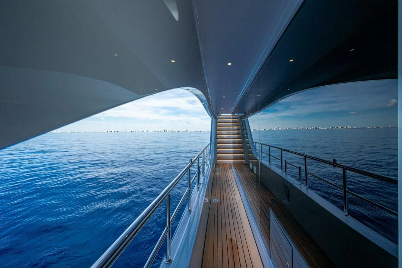 A sleek yacht exterior with a wooden deck and a staircase leading up, reflecting the serene blue ocean. aboard KING'S LAIR Yacht for Sale