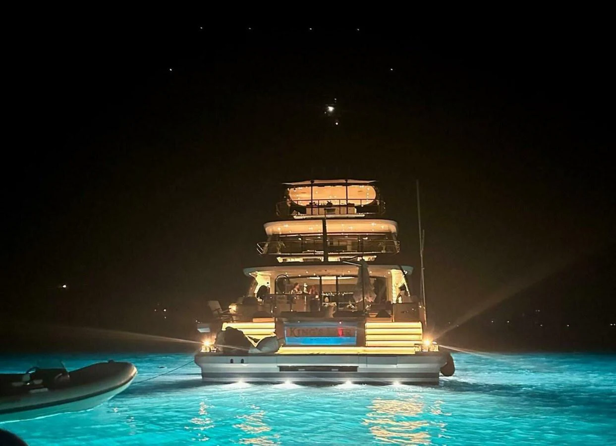 A luxurious yacht illuminated at night, anchored in glowing blue waters. aboard KING'S LAIR Yacht for Sale