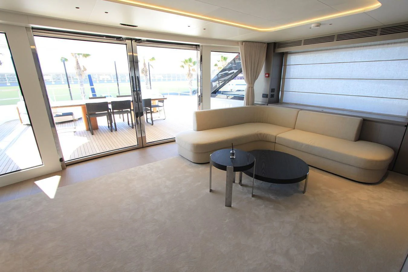 The spacious salon features a comfortable L-shaped sofa and a sleek coffee table, opening to an outdoor deck area. aboard OASIS 34M BO212 Yacht for Sale
