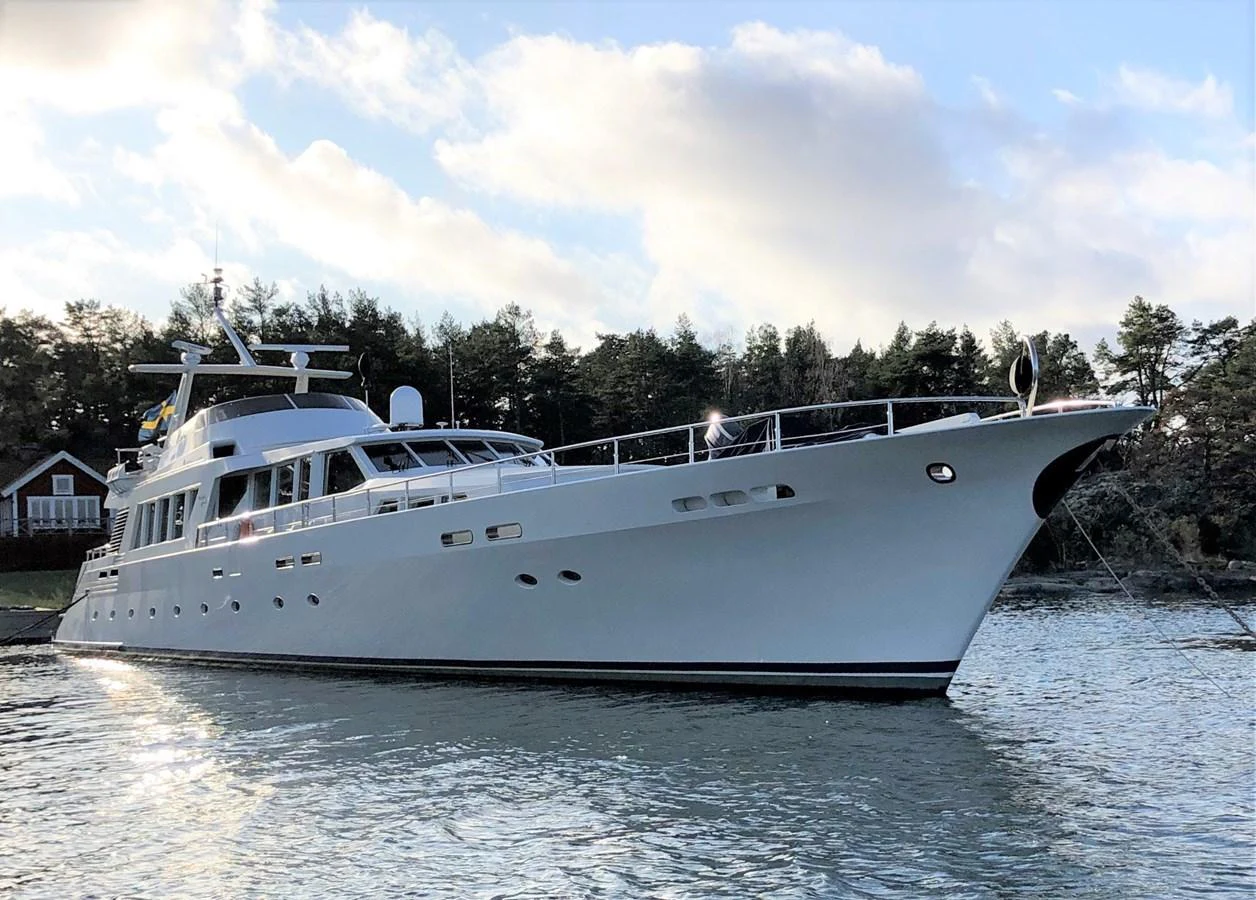 A sleek and elegant yacht is anchored near a scenic shoreline, showcasing its refined design and luxurious presence. aboard UNITED SPIRIT Yacht for Sale