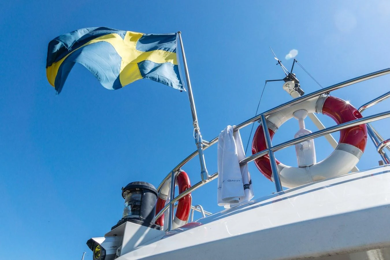 A close-up view of a yacht's deck featuring a flag, life ring, and towel against a clear blue sky. aboard UNITED SPIRIT Yacht for Sale