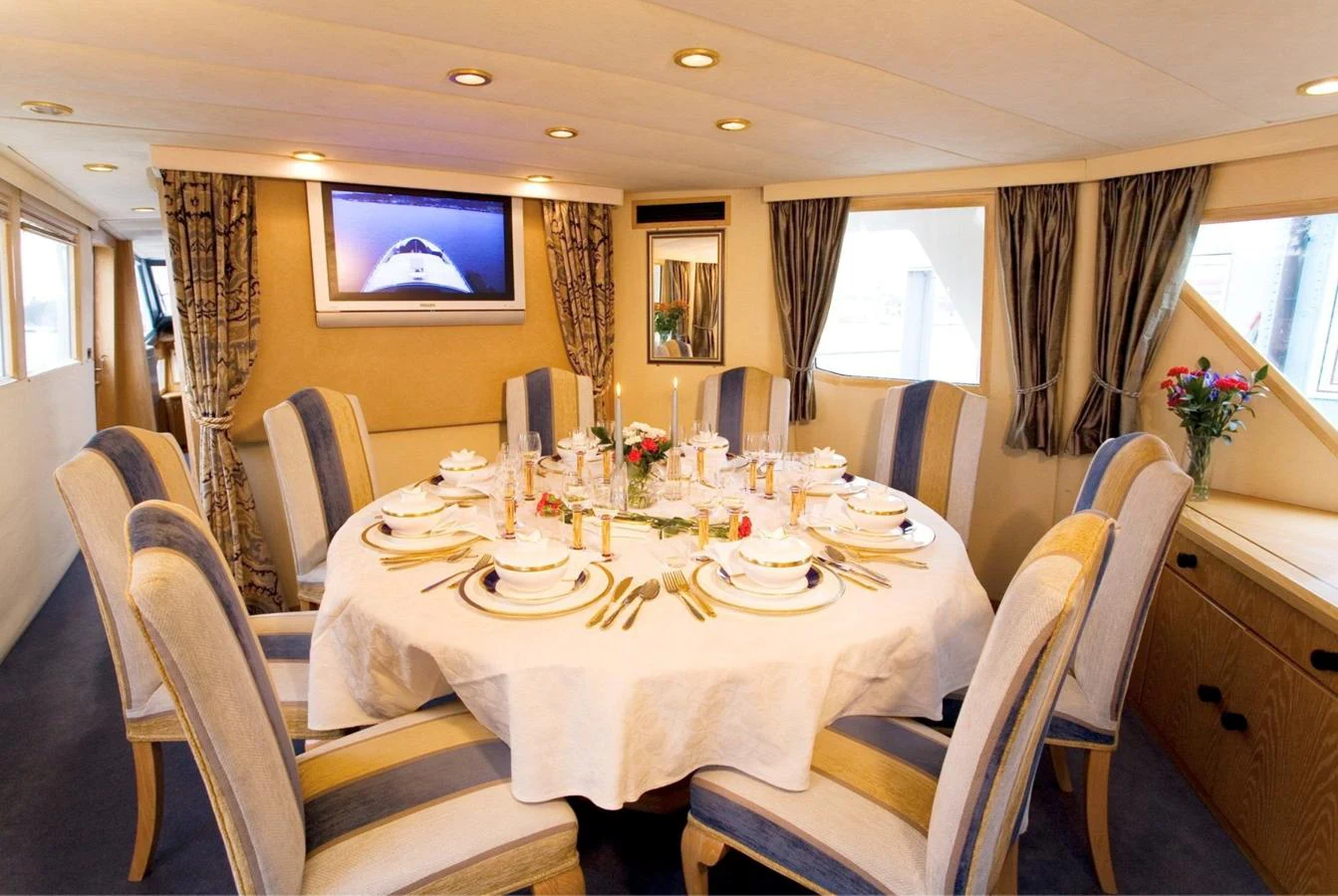 The yacht's dining area features an elegant round table set for a formal meal, surrounded by plush chairs and warm lighting. aboard UNITED SPIRIT Yacht for Sale