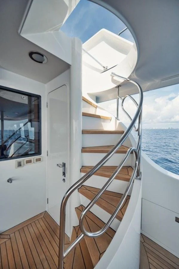 A sleek and modern staircase with wooden steps and stainless steel railings leads to the upper deck, offering a glimpse of the sea through the windows. aboard ISLAND GIRL Yacht for Sale