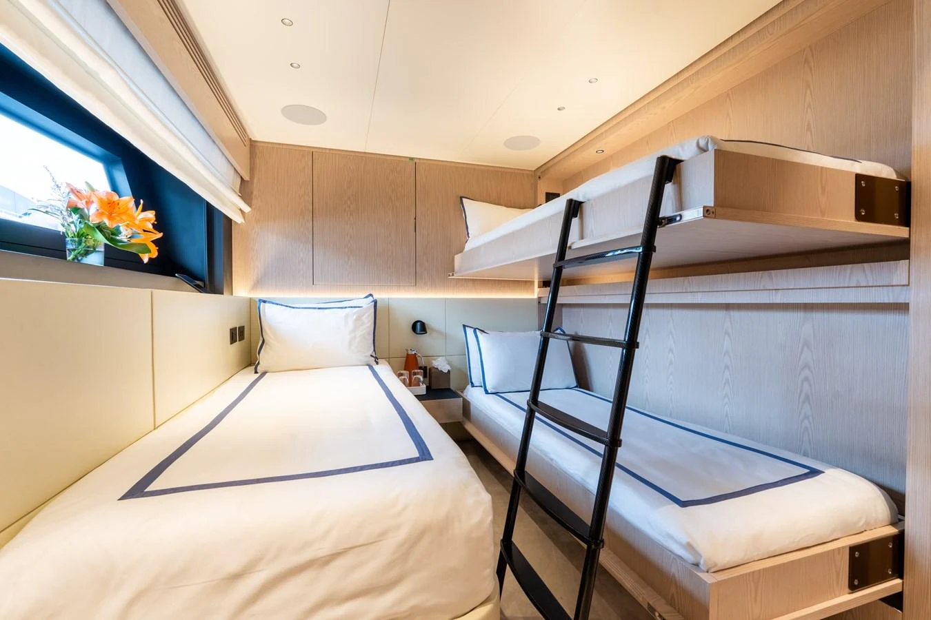 A cozy guest cabin with twin beds and a bunk bed, featuring modern decor and soft lighting. aboard A+ Yacht for Sale