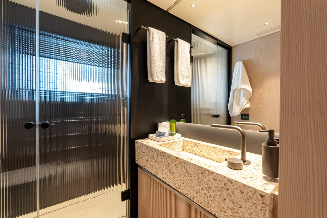 The bathroom features a modern design with a sleek sink and frosted glass shower door. aboard A+ Yacht for Sale