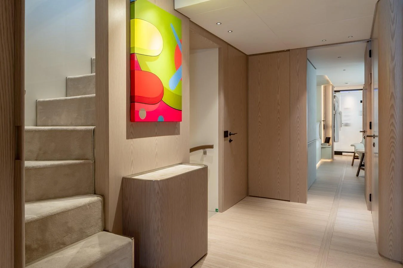 The yacht's interior features a modern hallway with light wood finishes and vibrant artwork. aboard A+ Yacht for Sale