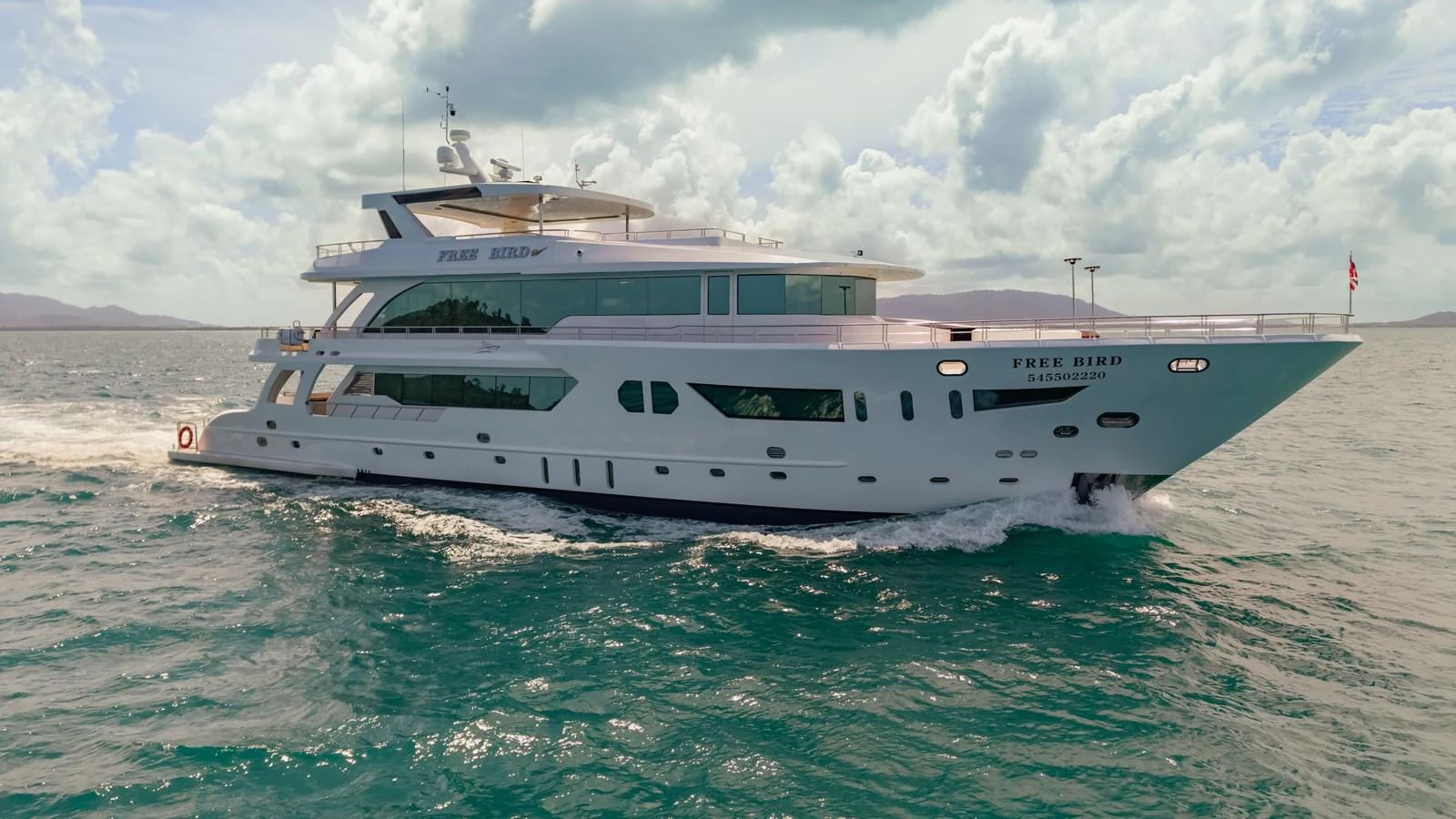 A luxurious yacht cruises through the open sea under a partly cloudy sky. aboard FREE BIRD Yacht for Sale
