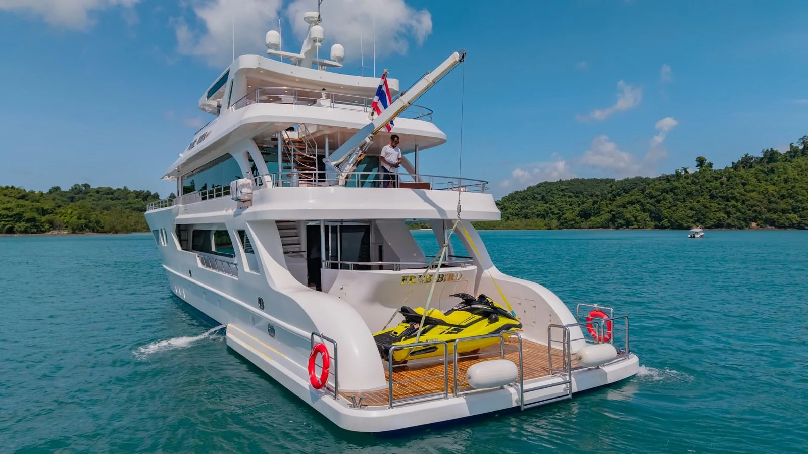 A luxurious yacht anchored in serene blue waters, featuring a spacious aft deck with jet skis. aboard FREE BIRD Yacht for Sale