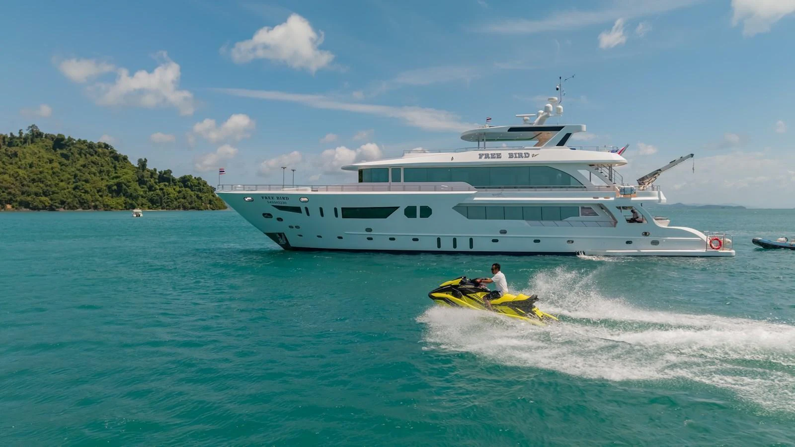 A luxurious yacht cruising on clear blue waters with a person riding a jet ski nearby. aboard FREE BIRD Yacht for Sale