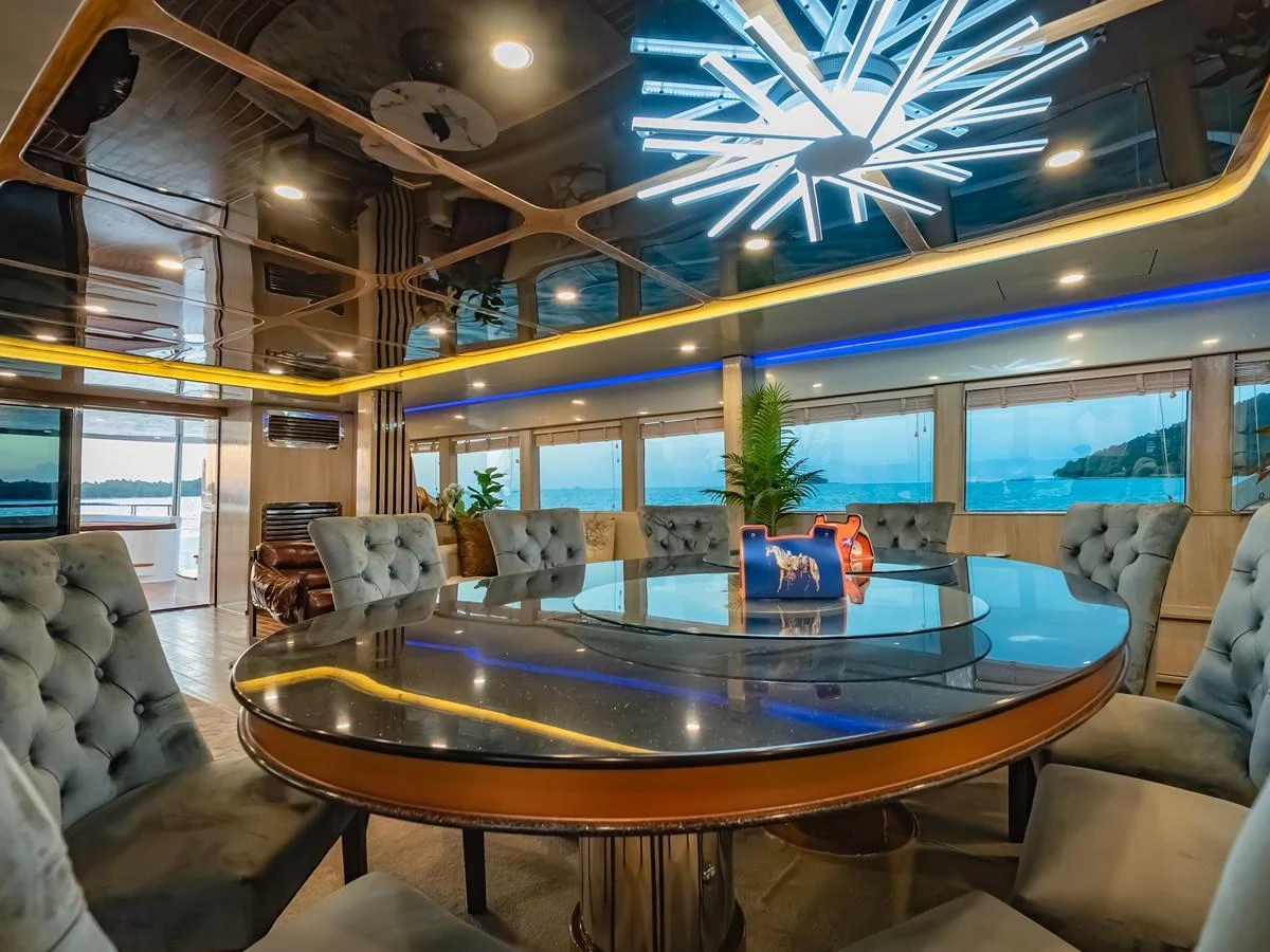 The yacht's dining area features a luxurious round table with plush seating and a modern chandelier, offering stunning views through large windows. aboard FREE BIRD Yacht for Sale
