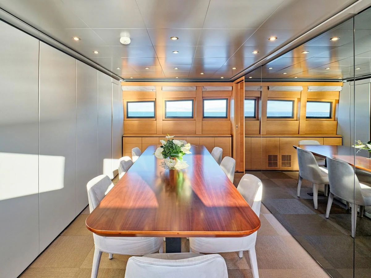 The yacht's dining area features a sleek wooden table surrounded by plush chairs, illuminated by natural light from the windows. aboard VENETICO Yacht for Sale