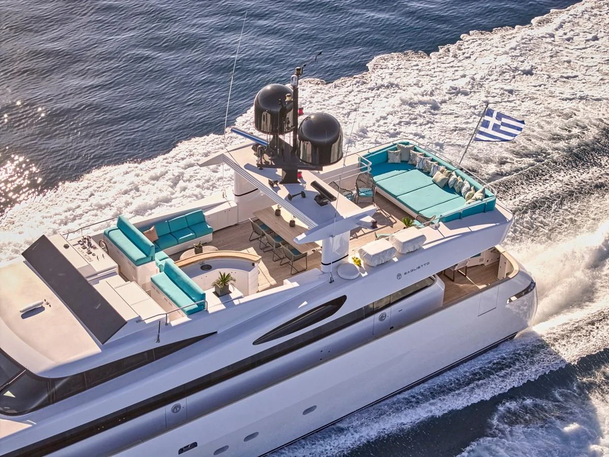 A luxurious yacht cruises through the water, showcasing its spacious flybridge with ample seating and a Greek flag waving at the stern. aboard VENETICO Yacht for Sale