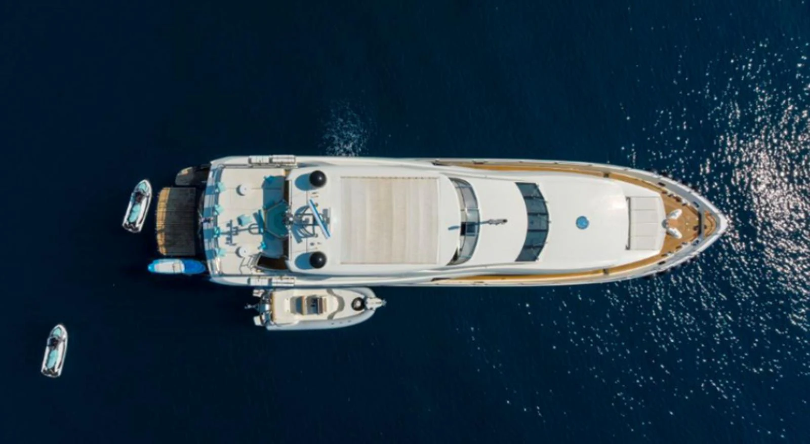 An aerial view of a luxurious yacht cruising on calm blue waters, accompanied by smaller boats. aboard ARAGO Yacht for Sale