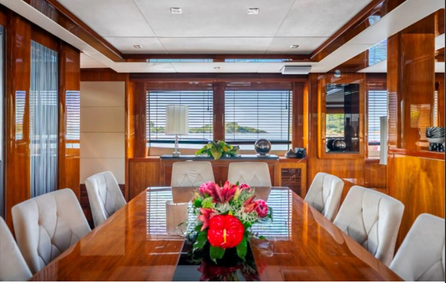 The yacht's dining area features a polished wooden table with plush seating and a centerpiece of fresh flowers, surrounded by large windows offering scenic views. aboard ARAGO Yacht for Sale