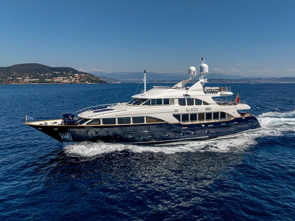 A luxurious yacht cruises through clear blue waters with a scenic coastline in the background. aboard SEA BLUEZ Yacht for Sale