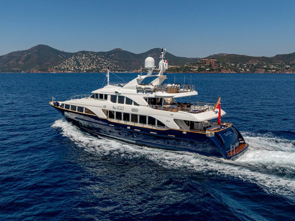 A sleek yacht cruises through clear blue waters with scenic hills in the background. aboard SEA BLUEZ Yacht for Sale