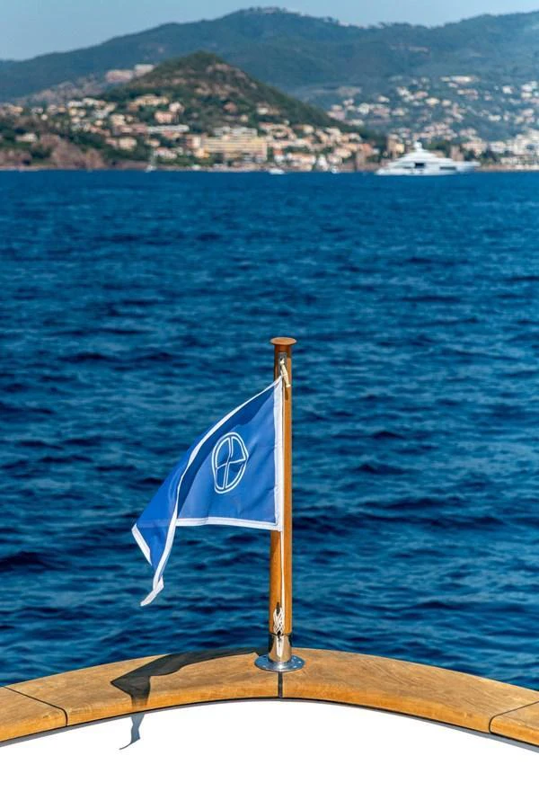 A close-up of a yacht's bow with a flag, set against a scenic coastal backdrop. aboard SEA BLUEZ Yacht for Sale