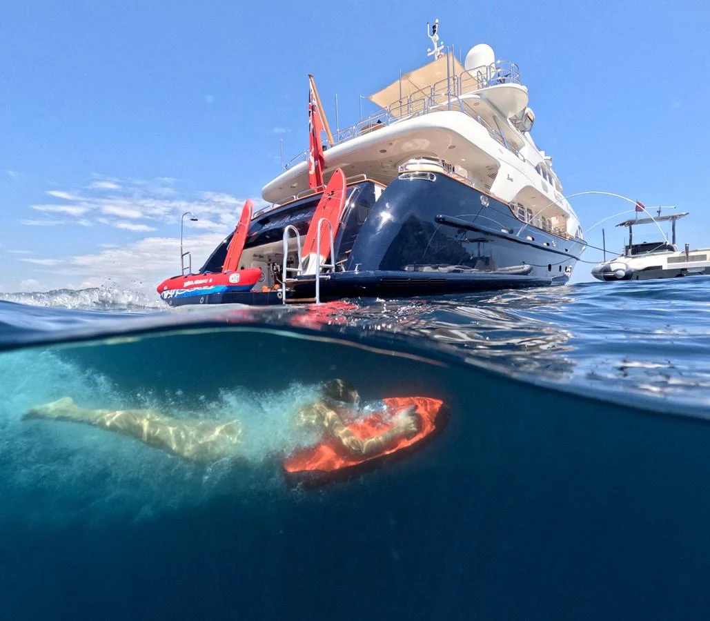 A luxurious yacht is anchored in clear blue waters, with a person swimming nearby. aboard SEA BLUEZ Yacht for Sale