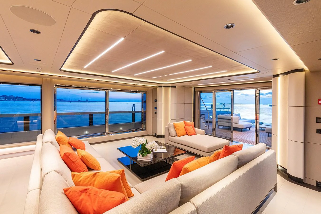 The spacious salon features plush seating with vibrant orange accents and expansive windows offering stunning ocean views. aboard DUCALE 120 Yacht for Sale