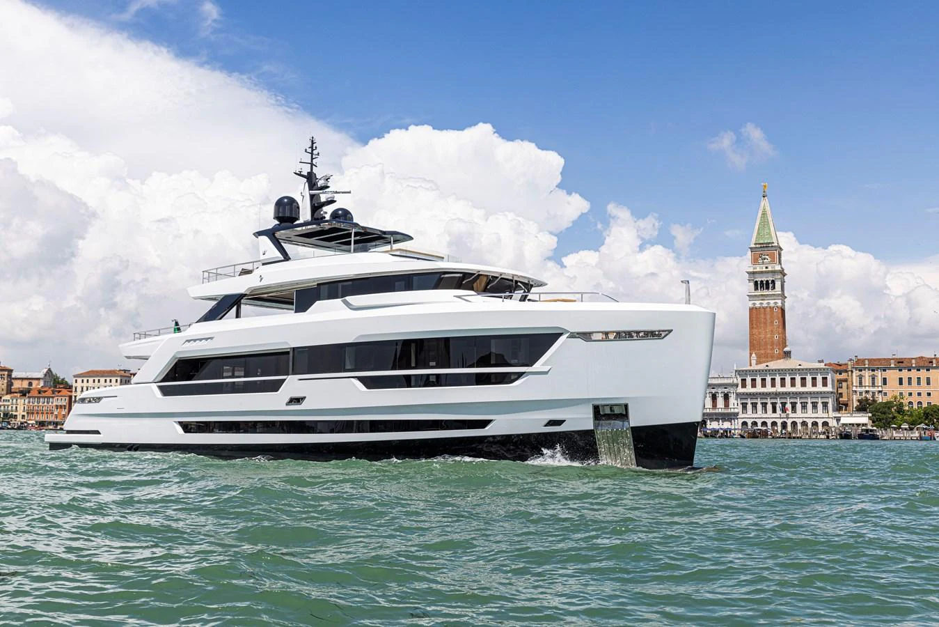 A sleek, modern yacht cruises through scenic waters with a historic cityscape in the background. aboard DUCALE 120 Yacht for Sale