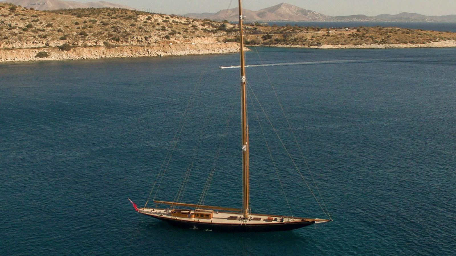 A sleek sailing yacht glides gracefully on calm blue waters with a scenic coastal backdrop. aboard CANDIDA Yacht for Sale