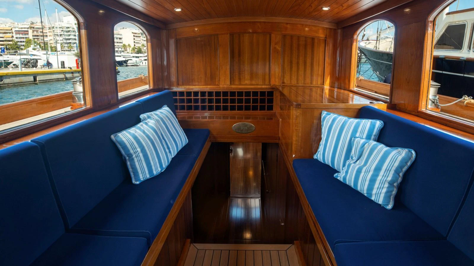 The cozy interior features rich wood paneling and plush blue seating with striped pillows, offering a warm and inviting atmosphere. aboard CANDIDA Yacht for Sale