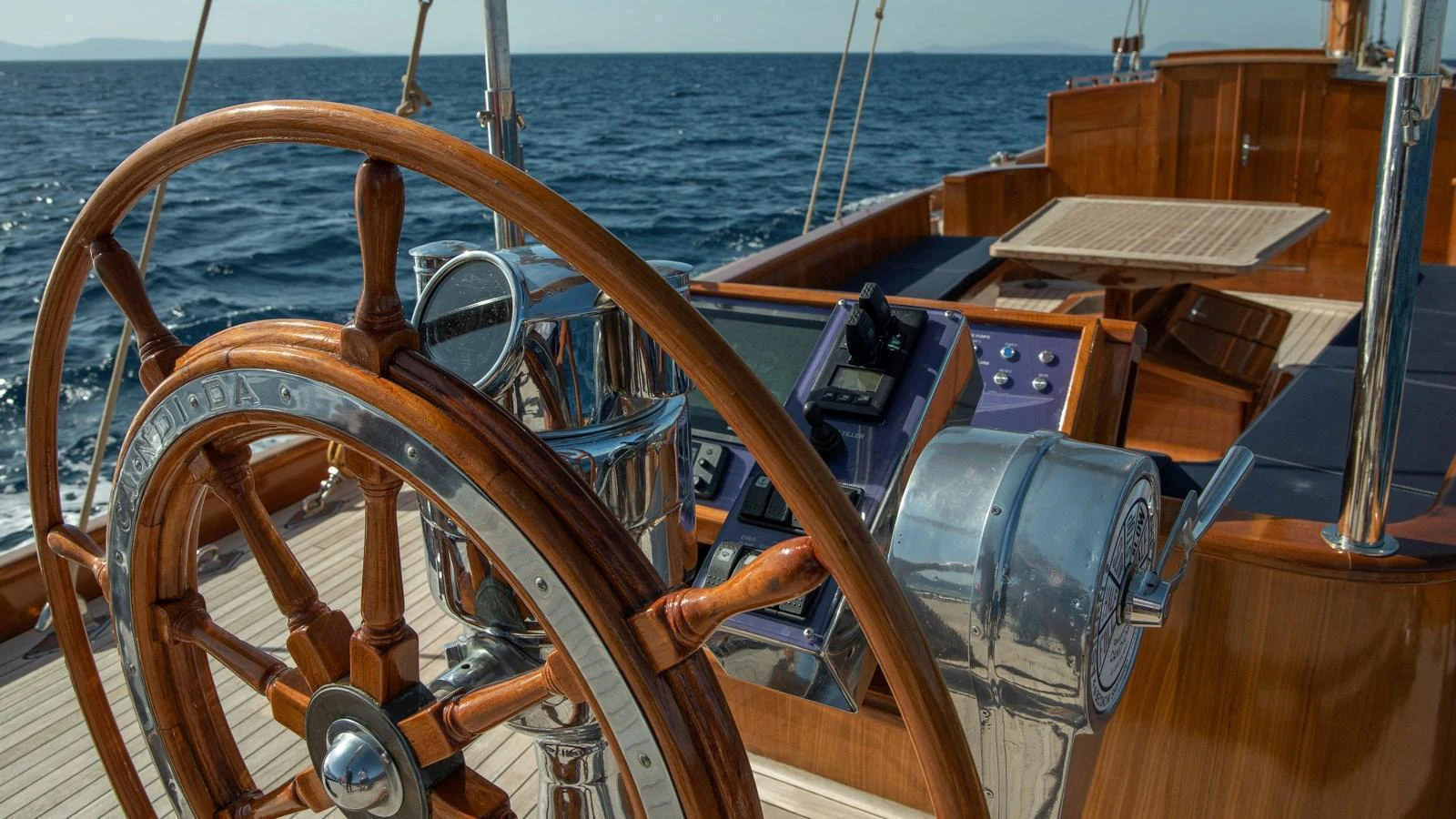 The yacht's helm showcases exquisite woodwork and advanced navigation instruments against a serene ocean backdrop. aboard CANDIDA Yacht for Sale