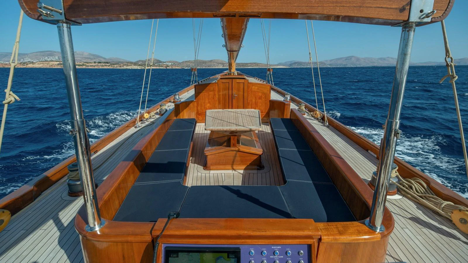 The yacht's deck features a spacious seating area with a central table, surrounded by polished wooden finishes and a stunning ocean view. aboard CANDIDA Yacht for Sale