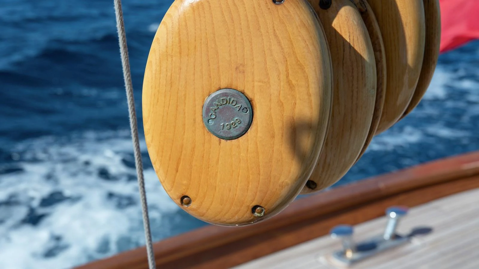 A close-up view of a wooden pulley system on a yacht, showcasing fine craftsmanship against a backdrop of the open sea. aboard CANDIDA Yacht for Sale