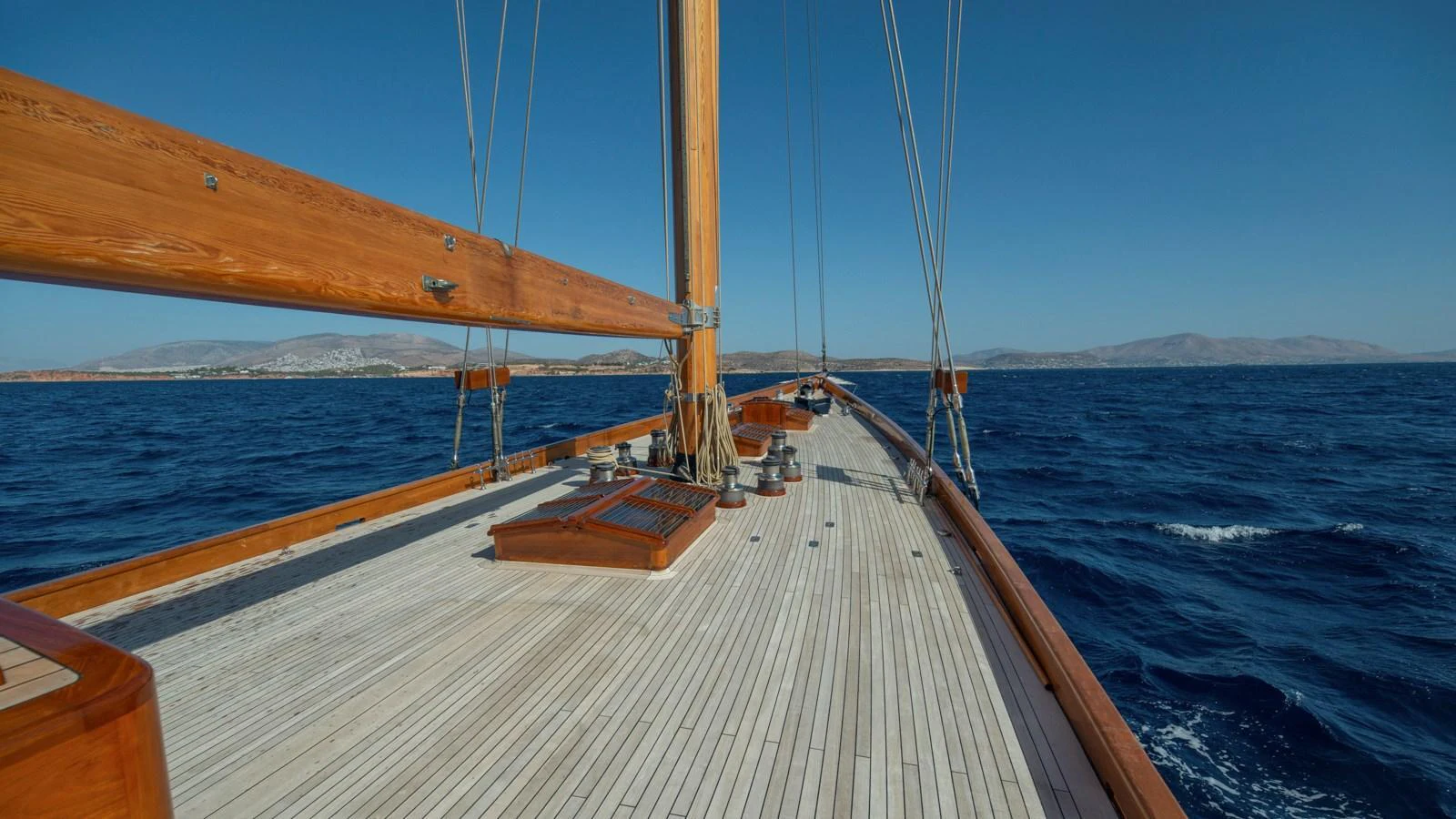 A classic wooden deck yacht sails smoothly on the open sea under a clear blue sky. aboard CANDIDA Yacht for Sale