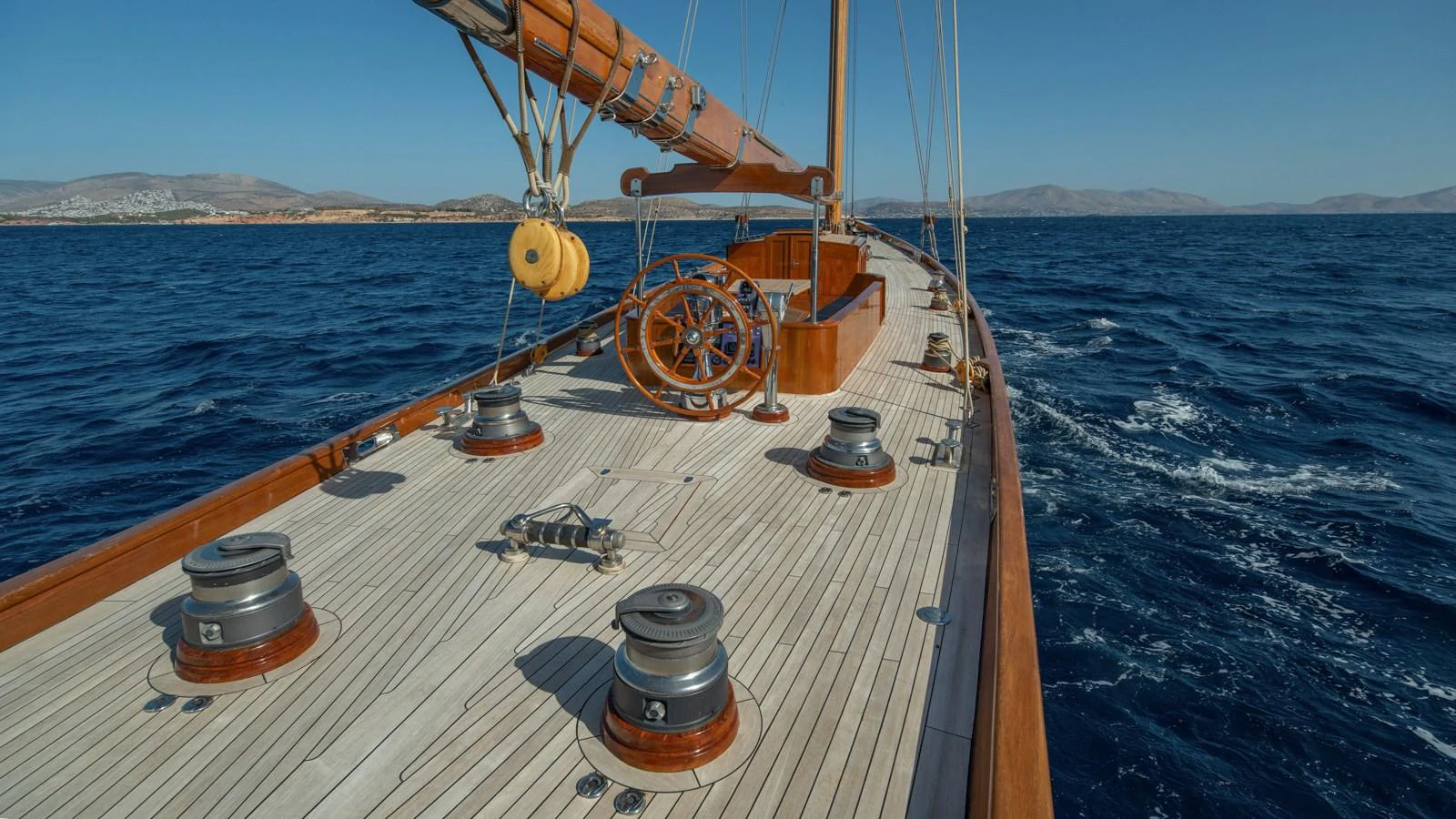 The yacht's deck showcases elegant woodwork and classic sailing elements against a serene ocean backdrop. aboard CANDIDA Yacht for Sale