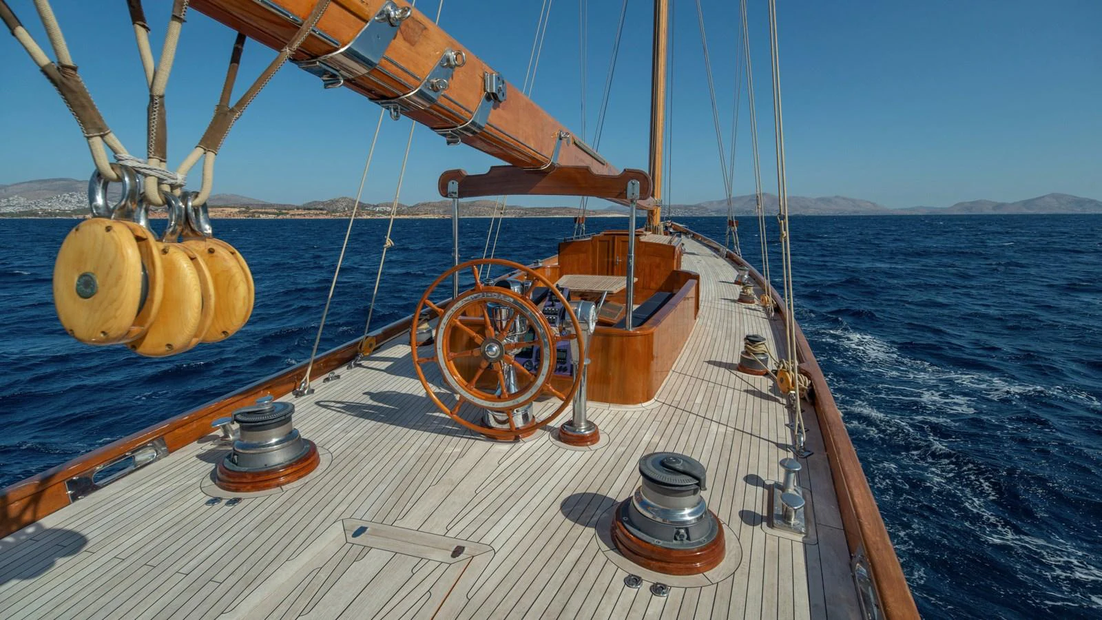 The yacht's deck showcases elegant wooden details and classic sailing equipment under a clear blue sky. aboard CANDIDA Yacht for Sale