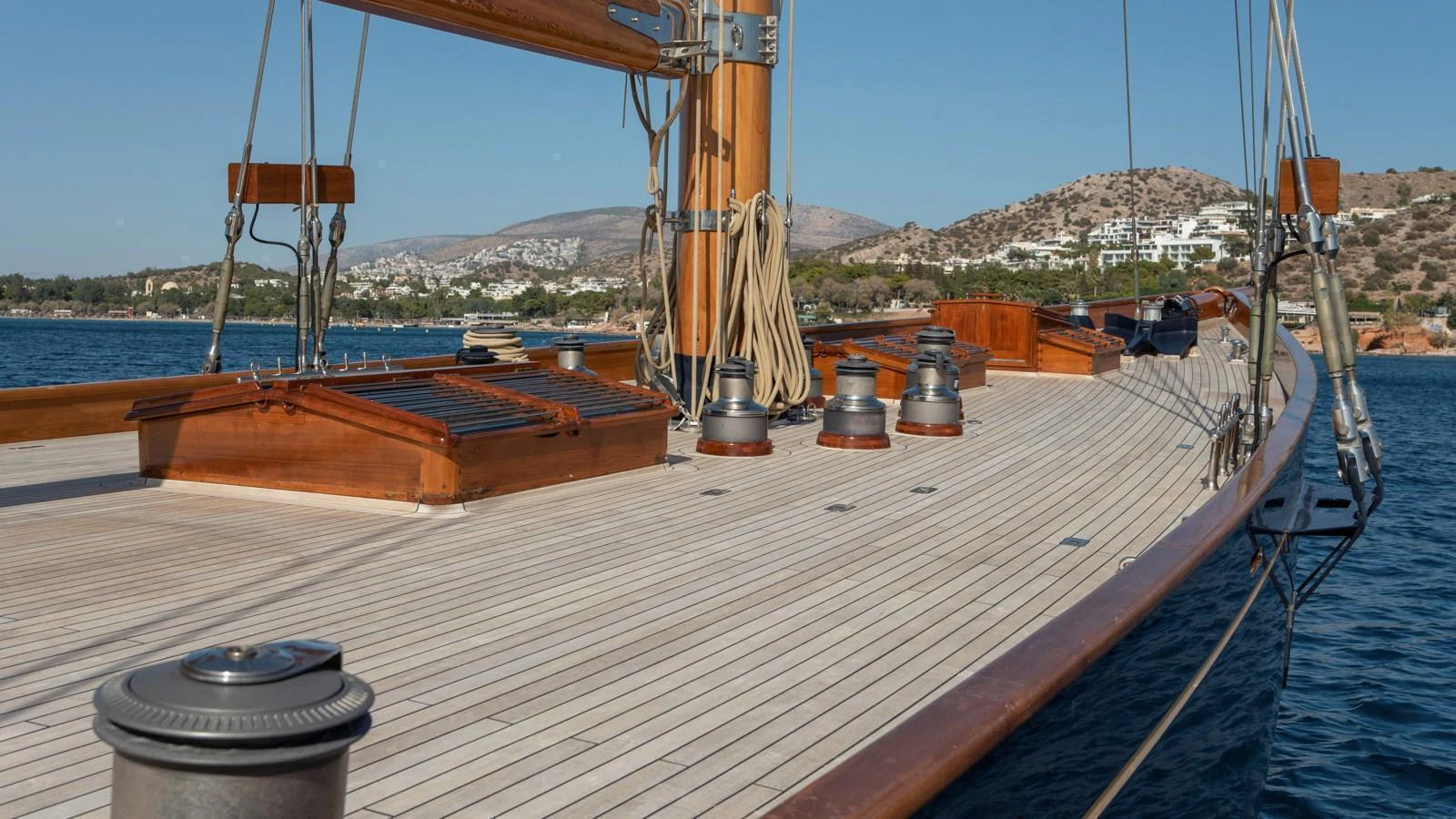 The yacht's deck showcases elegant wooden finishes and well-maintained rigging against a scenic coastal backdrop. aboard CANDIDA Yacht for Sale