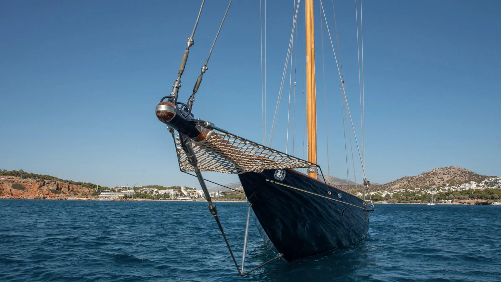 A classic sailing yacht with a sleek dark hull and wooden mast, anchored in serene blue waters. aboard CANDIDA Yacht for Sale
