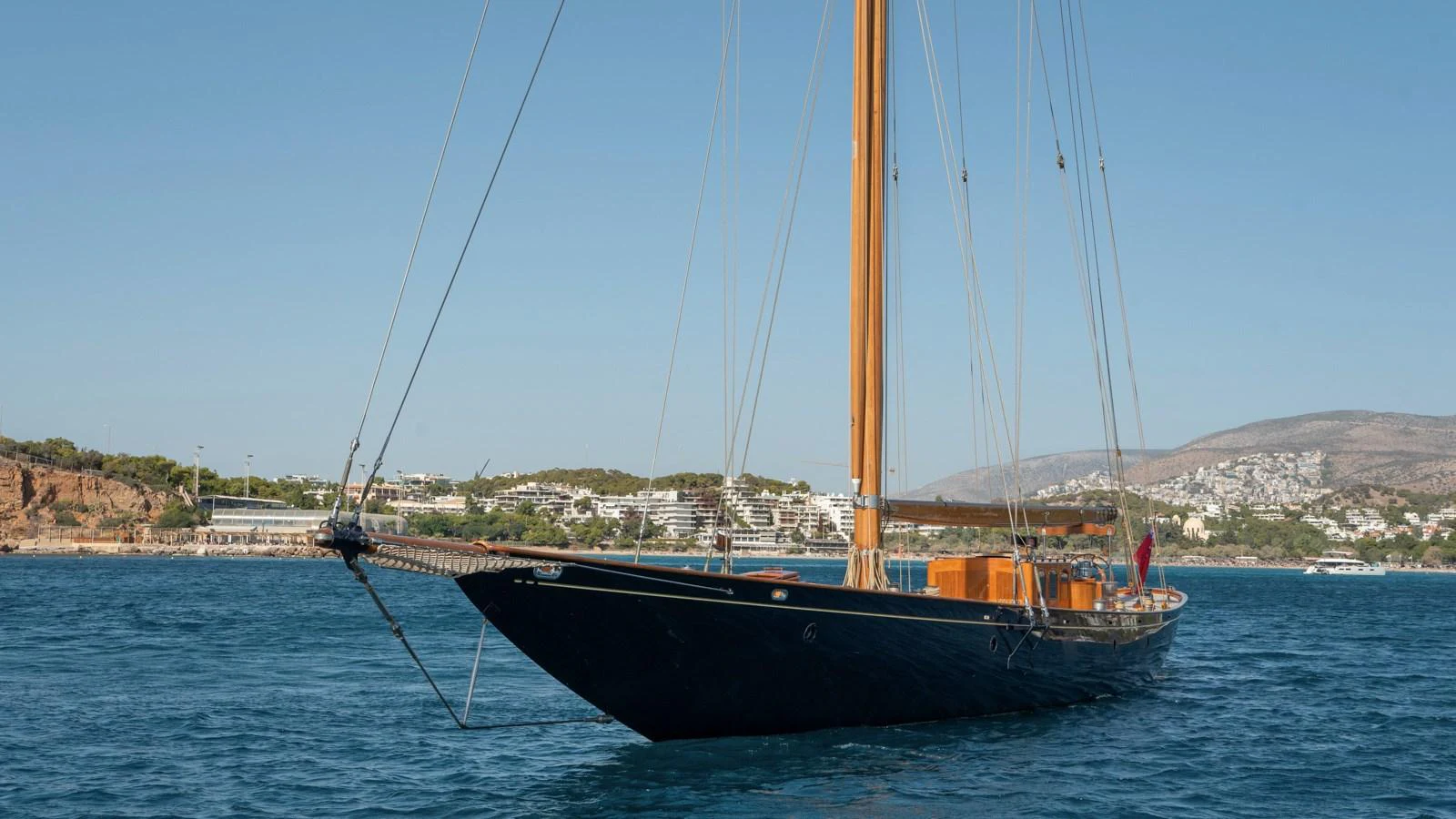 A classic sailing yacht with sleek lines is anchored in a serene coastal bay. aboard CANDIDA Yacht for Sale