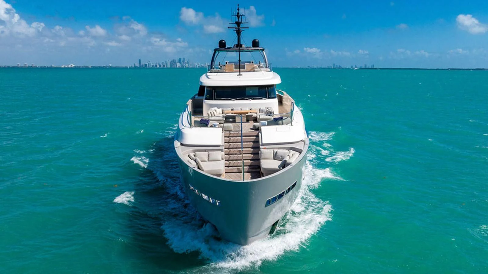 A luxurious yacht cruising through turquoise waters with a city skyline in the background. aboard SANLORENZO SD118/129 Yacht for Sale