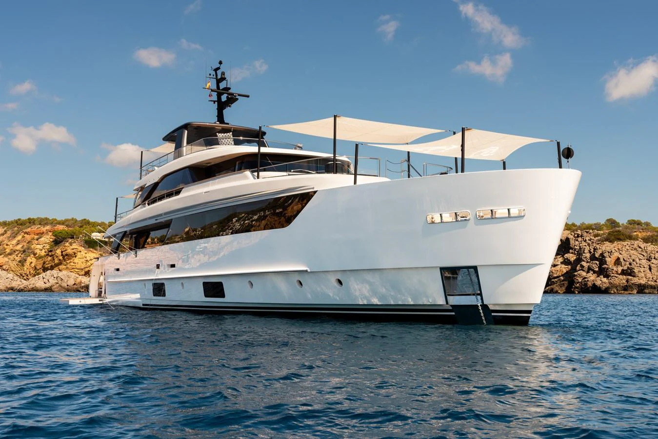 A sleek and modern yacht cruising in clear blue waters with a picturesque rocky coastline in the background. aboard AV1 Yacht for Sale