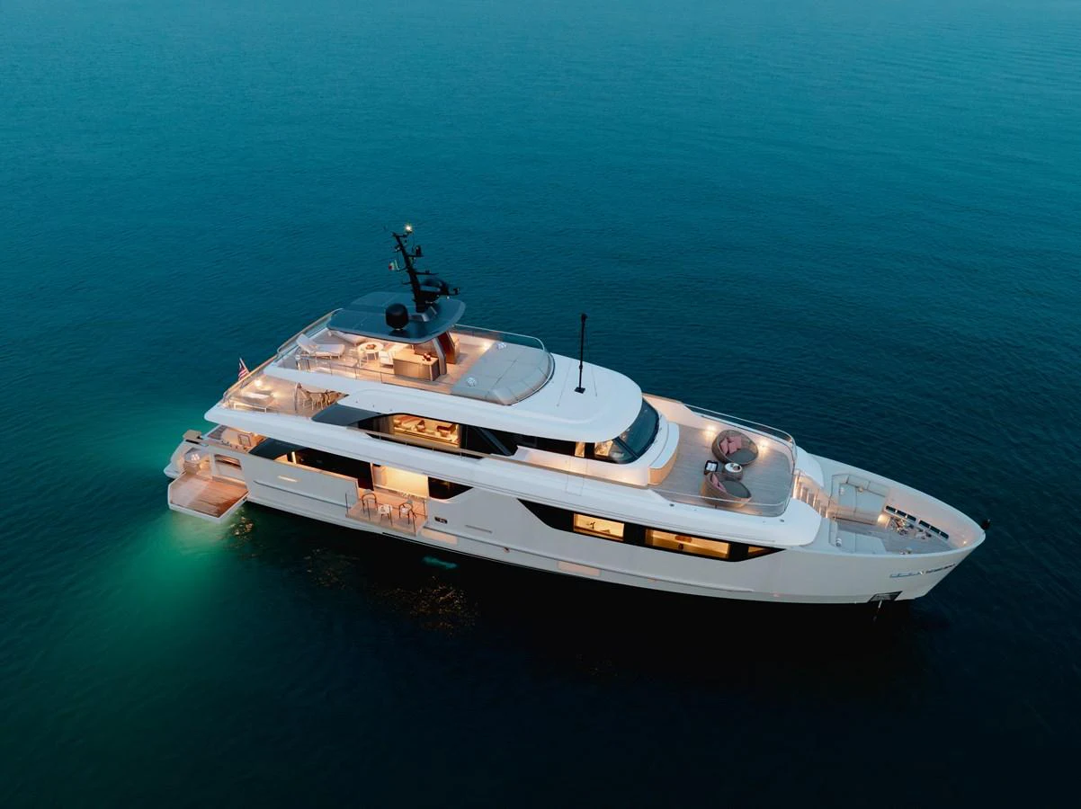 A luxurious yacht is anchored in calm waters, beautifully illuminated at dusk. aboard LET IT BE Yacht for Sale